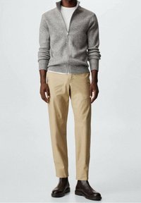 Suéter gris con cremallera y textura acanalada, combinado con pantalones beige de corte cónico y botines marrón oscuro. Diseño sencillo y clásico.