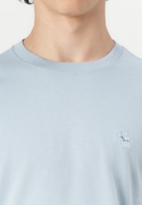 T-shirt à manches courtes bleu clair fabriqué en coton doux. Avec un col rond et un logo d'orignal brodé sur la poitrine.