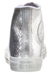 Vysoké stříbrné tenisky s texturovaným metalickým povrchem. Gumová podešev, bílé detaily a kulatý štítek na kotníku se sloganem "Converse All Star."