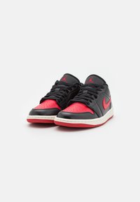 Scarpe da basket in pelle nere e rosse con punta perforata, intersuola bianca, suola rossa e lacci neri con logo rosso sui lati.