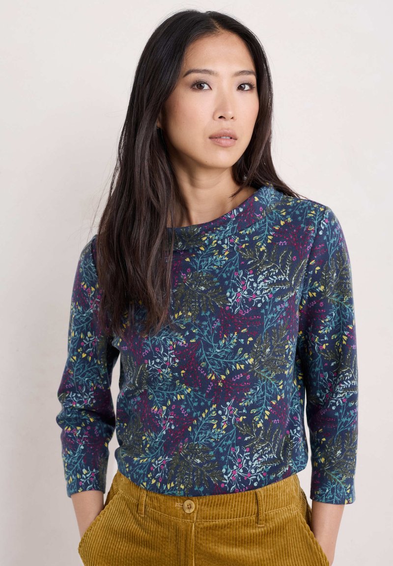 Top de manga larga en navy con un patrón floral en verde azulado, amarillo y rojo. Tejido suave con escote redondo y silueta ajustada.