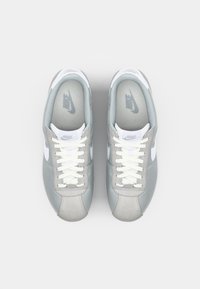 Grey sneakers with suede and mesh upper, white accents, and laces. Nike logo on tongue and side, round toe with textured rubber sole.