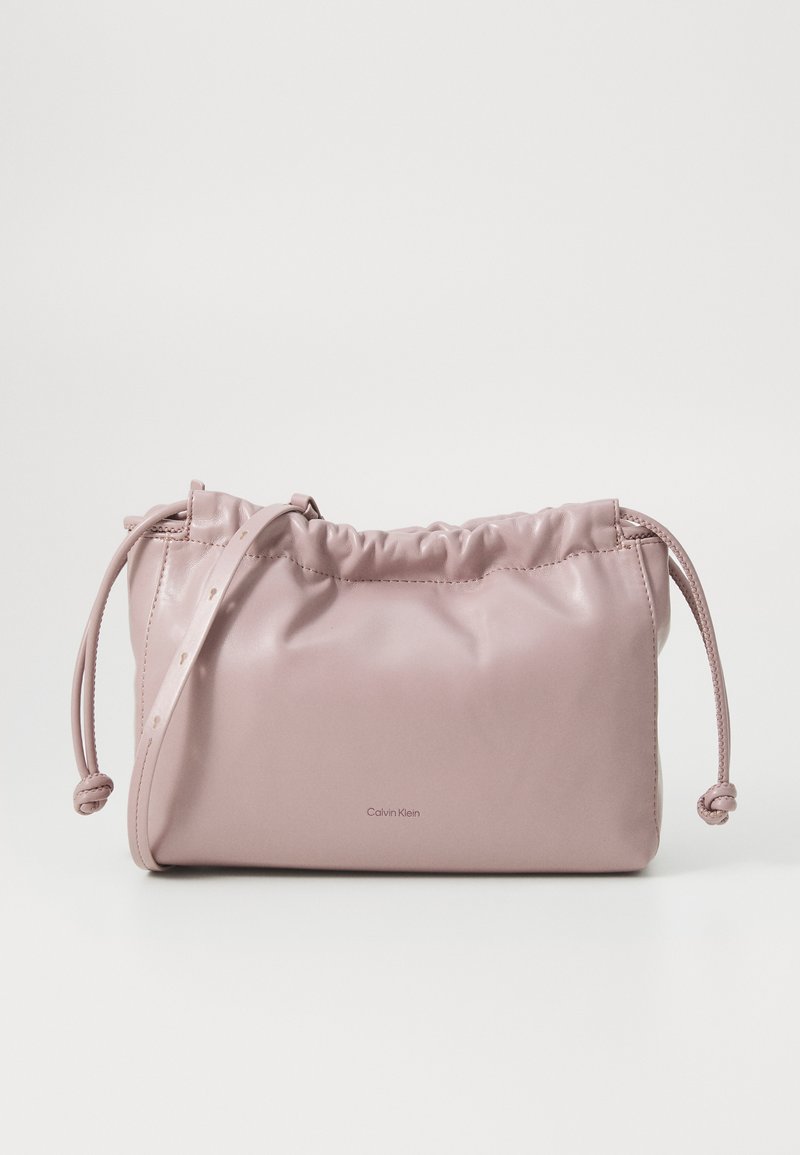 Borsa in pelle liscia di un rosa blush, con parte superiore arricciata, chiusura a coulisse e una cinghia sottile. Presenta un sottile logo Calvin Klein davanti.
