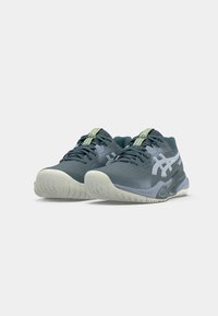 Sportssko med en mørkeblå overdel, perforeret design, limegrønne accenter og en tekstureret lys grå sål.