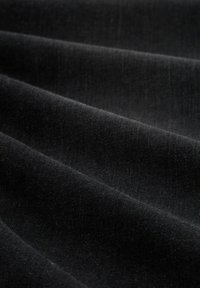 Tessuto nero con una consistenza morbida e liscia, caratterizzato da sottili variazioni di luce e ombra attraverso pieghe fluide.