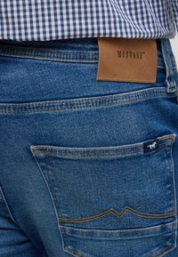 Jeans dżinsowe w niebieskim odcieniu, z skórzaną metką marki i dwiema tylnymi kieszeniami z żółtym przeszyciem oraz małą metką z logo.