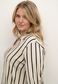 Crèmeblouse met zwarte verticale strepen, een kraag en knoopsluiting aan de mouwen, gemaakt van een lichte, soepele stof.