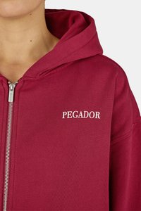 Burgundinė džemperis su užtrauktuku, pagamintas iš medvilnės. Baltu siūlumu ant krūtinės išsiuvinėtas žodis "PEGADOR". Šiame džemperyje yra reguliuojama gobtuvo virvutė.