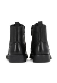 Cizme de gleznă negre din piele, cu o textură netedă, vârf rotunjit, fermoare laterale și detalii decorative de brogue pe spate.