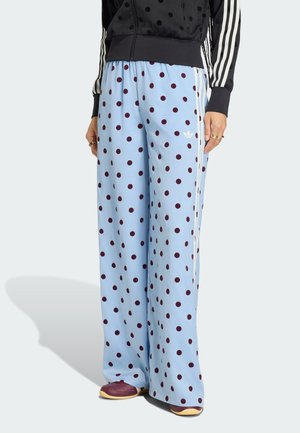 Světle modré kalhoty s širokými nohavicemi a vínovými puntíky, s bílými bočními pruhy, kombinované s vínovými botami a černou bundou s bílými pruhy.