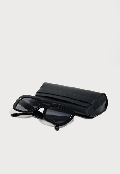 Lunettes de soleil rectangulaires noires avec des verres foncés, posées à côté d'un étui en cuir noir assorti sur fond blanc.
