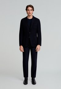 Blazer texturizado en color marino con dos bolsillos frontales, combinado con pantalones oscuros y botines negros. Diseño sencillo, corte entallado y tejido suave.