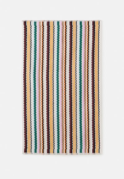 Serviette avec des rayures en zigzag verticales vert, jaune, marron, rose, noir et blanc sur fond blanc.