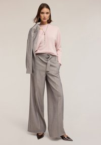 Maglione rosa con collo alto, pantaloni a gamba larga grigi con righe, vita con cintura, abbinati a tacchi a punta neri e un blazer grigio.