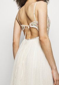 Bílé šaty s květinovou výšivkou na zadní straně, průhlednou látkou s puntíky, nastavitelnými ramínky a zavazovací šňůrkou v pase.