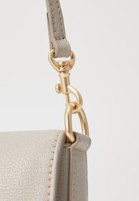 Borsa a tracolla in pelle grigia chiara con hardware dorato, caratterizzata da una superficie testurizzata e una tracolla collegata da una chiusura rotonda.