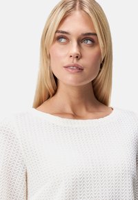 Weißer strukturierter Pullover mit gewelltem Muster, ausgestattet mit einem weiten Rundhalsausschnitt und weichem, leichtem Strickstoff.