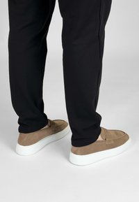 Tan suède instappers met een witte rubberen zool, met een gestructureerde afwerking en een minimalistisch design, gecombineerd met zwarte broeken.