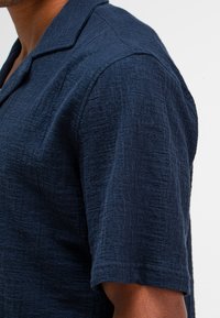 Korte mouwen overhemd in een gestructureerde marineblauwe stof met een kraag. Heeft een subtiel patroon, een getailleerde pasvorm en een gladde, geweven textuur.