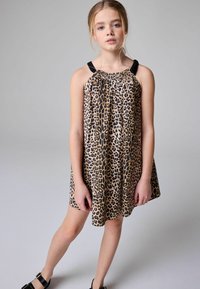 Haljina s leopard uzorkom, crnim trakama, lepršavog dizajna i nabranim dekolteom. Glatka tkanina, do koljena, ležeran kroj, nošena uz crne sandale.