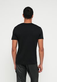 Fekete pamut rövid ujjú póló kerek nyakkivágással, hátulnézetből, fekete texturált nadrággal párosítva. Egyszerű és testhezálló kialakítás.