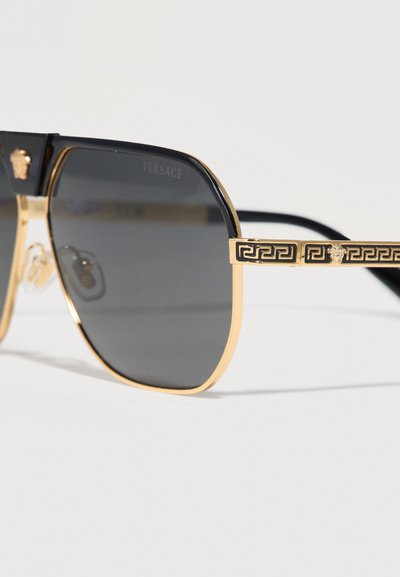 Μαύρα και χρυσά γυαλιά ηλίου Versace με τετράγωνα σκούρα φακούς, χρυσά γεωμετρικά μοτίβα στα πλαϊνά και λεπτομέρειες με το λογότυπο κεφαλής Μέδουσας.