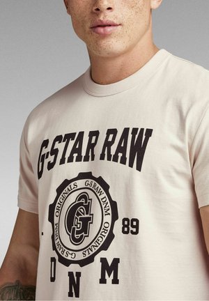 Lichtbeige katoenen t-shirt met een groot zwart grafisch logo met de tekst "G-STAR RAW" en decoratieve cirkelaccenten.