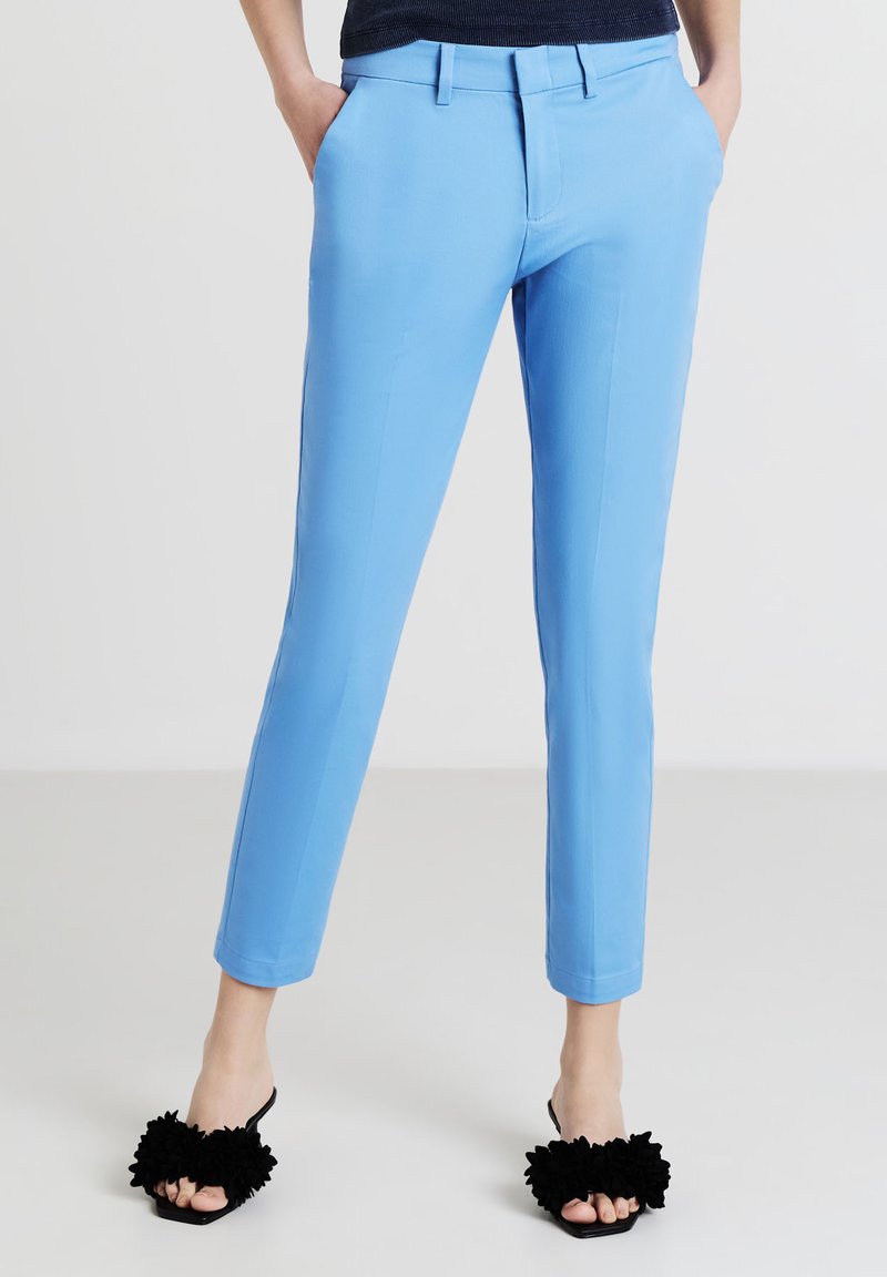 Pantaloni su misura blu chiaro dal taglio slim, con passanti per la cintura e tasche. Indossati con sandali neri a slide con accenti floreali.