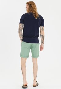 Laivansininen puuvillapaita yhdistettynä vaaleanvihreisiin shortseihin, joita koristavat käärityt helmavarat. Shortseissa on sivutaskut ja rento istuvuus.