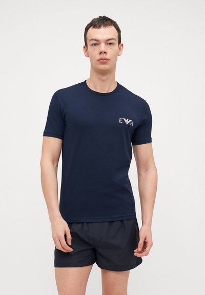 T-shirt en coton bleu marine avec un col rond et des manches courtes, featuring un logo blanc imprimé sur le côté gauche de la poitrine.