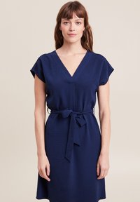Marineblaues Kleid mit V-Ausschnitt, kurzen Ärmeln und einem Gürtel in der Taille. Hergestellt aus strukturiertem Stoff, bietet es eine lockere Passform und eine knielange Schnittform.