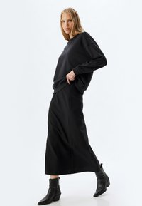 Felpa nera oversize con sottili accenti brillanti, abbinata a una gonna maxi nera aderente e stivali neri alla caviglia.