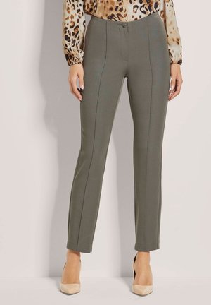 Olivgrüne maßgeschneiderte Hose mit glatter Textur, geradem Bein Design und Vordernahtdetails, kombiniert mit einer gemusterten Bluse und beigen Absätzen.