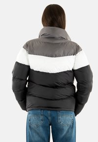 Giacca imbottita con colletto alto, in blocchi di colore nero, grigio e bianco. Tessuto testurizzato con finitura lucida, indossata con jeans blu.