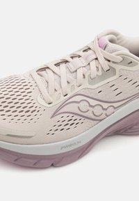 Baskets de course rose clair avec une tige en mesh, présentant un design en forme de vague de rose plus foncé, une semelle intermédiaire blanche et une semelle lavande texturée.