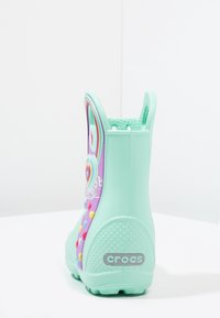 Botte imperméable vert menthe avec un côté violet vif arborant un motif arc-en-ciel et des boutons en forme de cœur colorés. Comprend une semelle texturée.