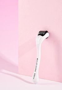 Derma roller med 0,5 mm svarta mikronålar och ett vitt plasthandtag, placerad mot en rosa bakgrund. Slät yta, ergonomisk design.