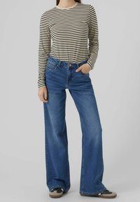 Camisa de manga larga a rayas en color crema y negro, combinada con unos vaqueros de pierna ancha en azul. Los vaqueros tienen una cintura alta y un sutil detalle en los bolsillos. Zapatillas marrones.