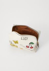 Trousse à maquillage en cuir blanc ornée d'illustrations fantaisistes, comprenant des cerises et un papillon, avec une fermeture éclair dorée et un intérieur brun.