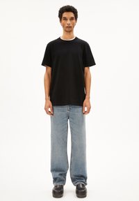 T-shirt en coton noir avec un col rond, associé à un jean en denim bleu clair à coupe ample et des sabots noirs épais. Design simple, style minimaliste.