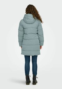 Svijetloplava пухersка jakna s kapuljačom, quilted dizajn i podesivim vezicama, kombinirana s tamnim trapericama i crnim čizmama.
