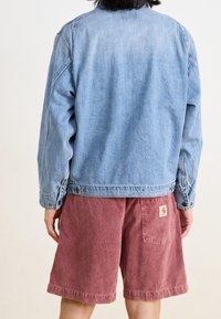 Lichtblauwe spijkerjack met een relaxed fit, voorzien van een knoopsluiting bij de kraag en gedetailleerde stiksels, gecombineerd met bordeauxrode corduroy shorts.