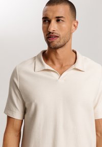 Camisa polo de canalé beige con un cuello en V y mangas cortas, que presenta una textura suave y un corte relajado.