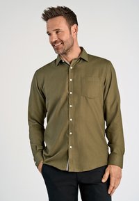 Olivegrünes Langarmhemd mit Knopfleiste, Tasche auf der linken Brust und weißen Knöpfen. Der Stoff hat eine strukturierte Oberfläche.