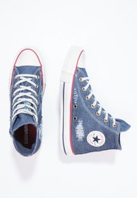 Džínové vysoké tenisky s opotřebovanými detaily, bílou gumovou špičkou a oky, se červenými a modrými pruhy na podrážce.