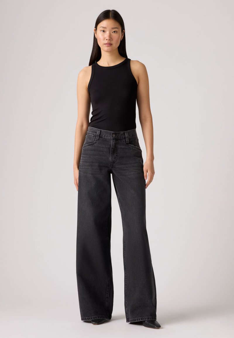 Débardeur noir côtelé associé à un jean noir ample et taille haute. Le jean comporte une fermeture à boutons et des poches latérales ; les deux ont une texture lisse.