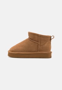 Brune suedette ankelstøvler med rund tå, enkelt design, lav profil og en bakre trekkhjul for enkel påkledning. Myk innvendig fôr synlig.