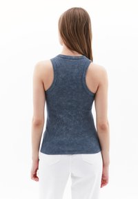 Mørkeblå tætsiddende top med ribbet tekstur, brede skulderremme og rund udskæring, parret med hvide jeans og subtile detaljer på ryggen.