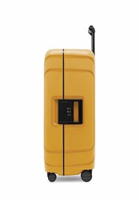 Valise rigide jaune avec serrure intégrée noire, quatre roues et poignée télescopique étendue vue de côté.