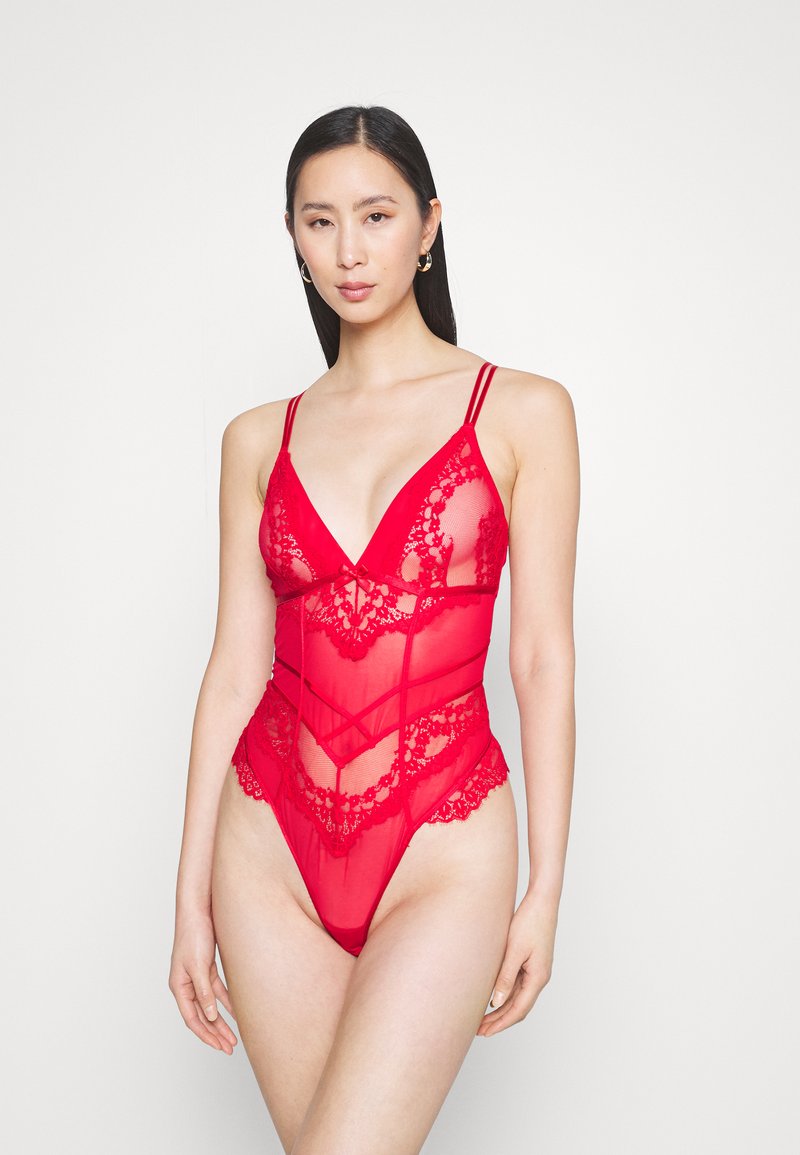 Rød blonde bodysuit med gjennomsiktige mesh-paneler, en dyp utringning og intrikat blonde-detaljering langs kantene og mønstrene.